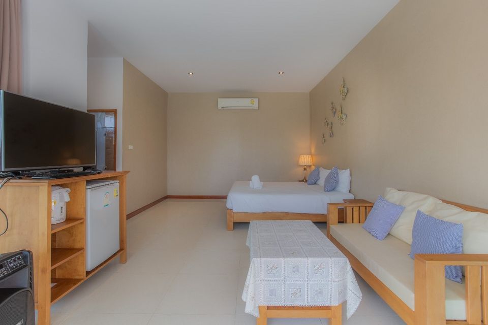 Bright bedroom with wooden furniture at Proud V Pool Villa, Hua Hin. Features a bed, sofa, TV, and mini-fridge.