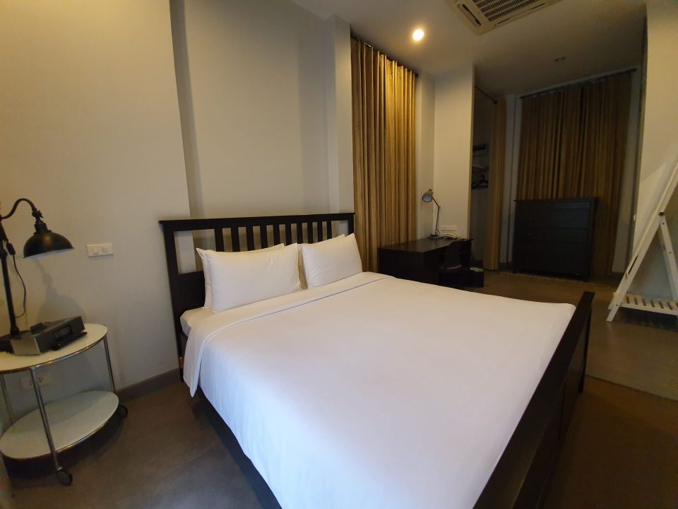 Bedroom with king bed at Sala Haven Nine Pool Villa, South Pattaya. Neutral color scheme, bedside table with lamp.