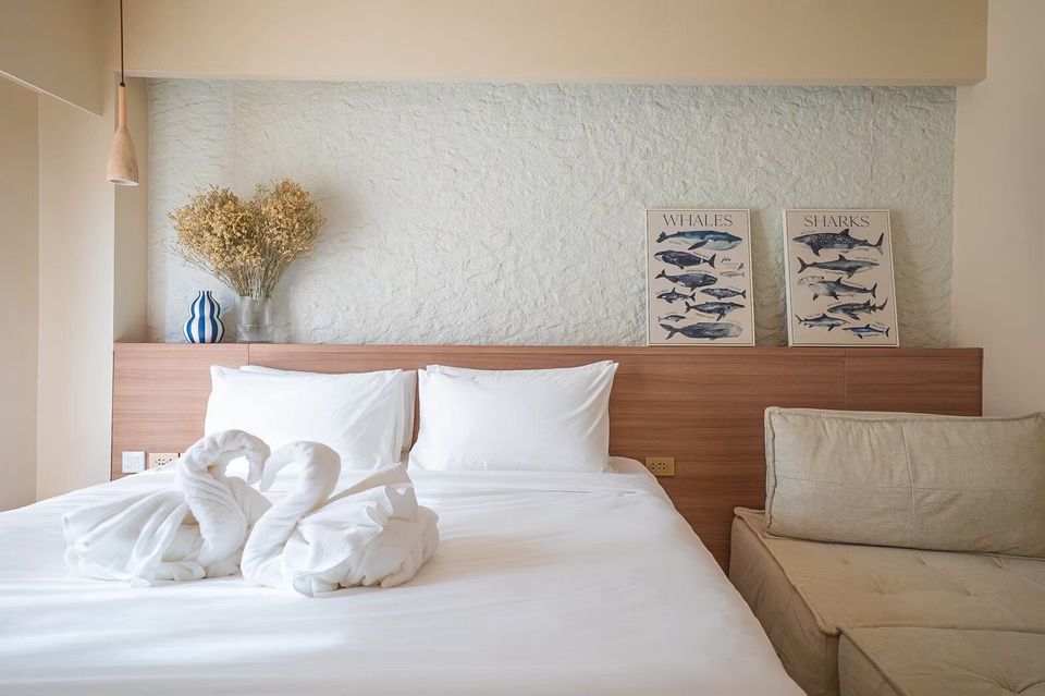 A king-size bed with white linens and towel swans in a bedroom at Sand Moment VI Pool Villa, Rayong. Whale and shark art on wall.