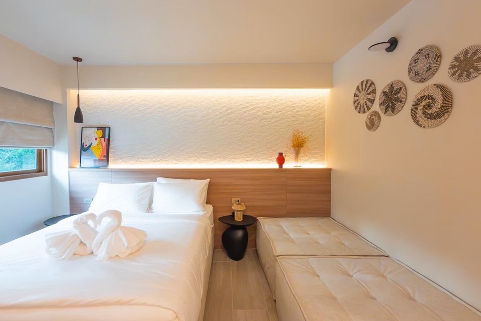 A minimalist bedroom at Sand Moment VI Pool Villa, Rayong, featuring a twin bed with swan towels and a long daybed.