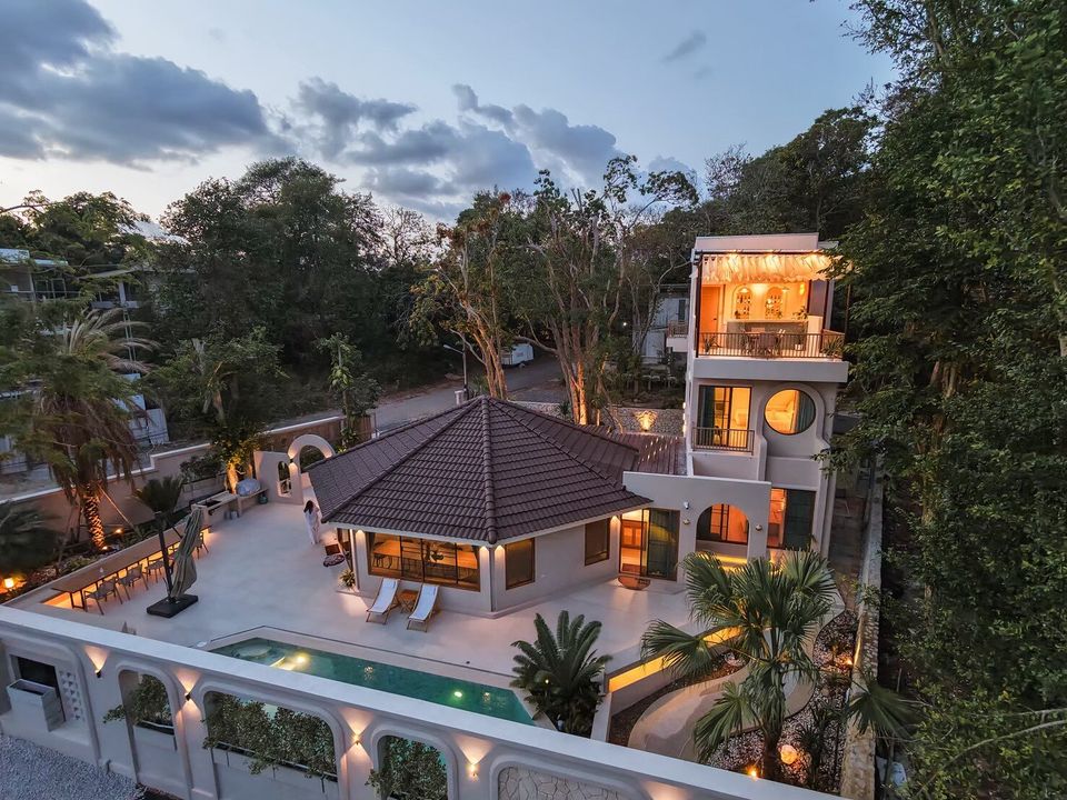 Aerial view of Sand Moment VI Pool Villa in Rayong at dusk, showcasing the illuminated exterior, pool, and surrounding trees.