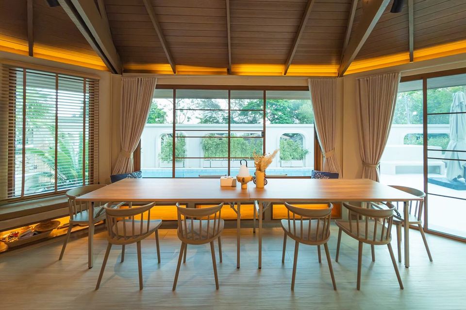 Elegant indoor dining area at Sand Moment VI Pool Villa, Rayong, with a long wooden table, chairs, and a view of the pool.