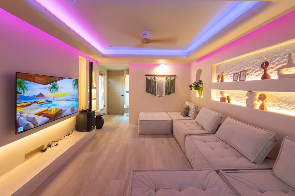 Modern living room at Sand Moment VI Pool Villa, Rayong, featuring a large TV, comfortable sofa, and colorful mood lighting.