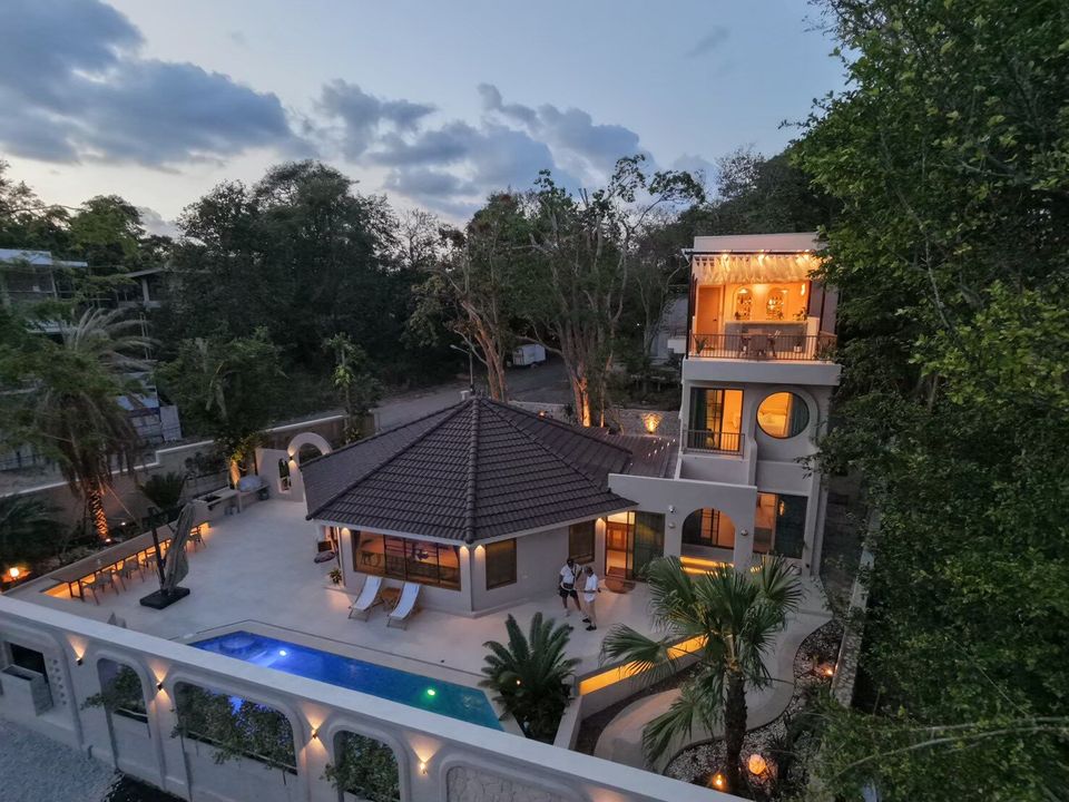 Aerial dusk view of Sand Moment VI Pool Villa in Rayong, showcasing the illuminated exterior, pool, and surrounding lush trees.