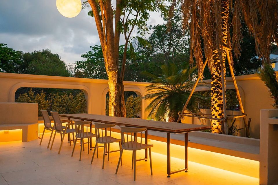 Outdoor dining area at Sand Moment VI Pool Villa, Rayong, with a long wooden table, chairs, and warm ambient lighting at dusk.