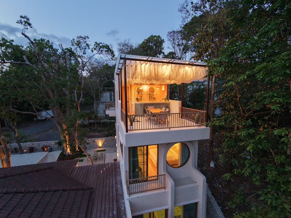Aerial view of Sand Moment VI Pool Villa in Rayong at dusk, showcasing its multi-level design with a rooftop bar and balcony.