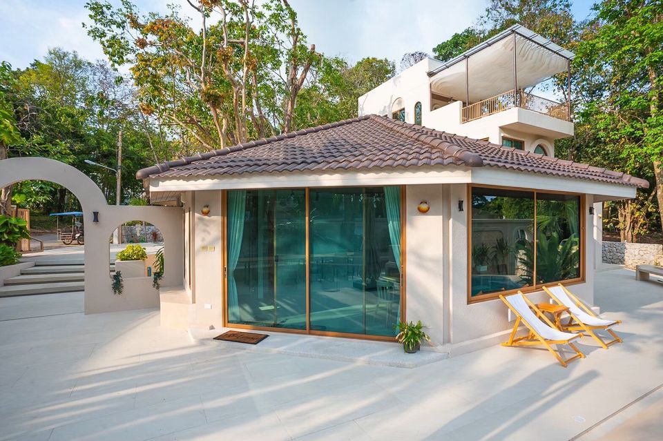 Daylight view of Sand Moment VI Pool Villa entrance in Rayong, featuring arched walls, tiled roof, and lush greenery.