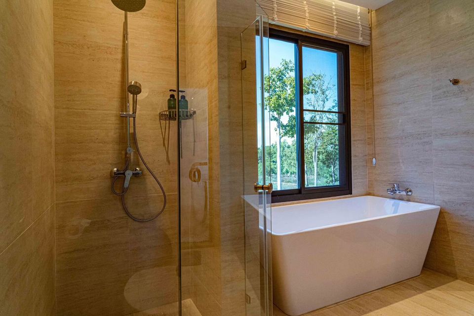 Modern bathroom at Sea Moment IV Pool Villa, Rayong, featuring a freestanding bathtub and a spacious rain shower with glass enclosure.