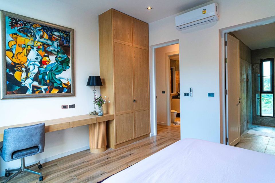 Modern bedroom at Sea Moment IV Pool Villa, Rayong, featuring a desk, wardrobe, and vibrant abstract art. Ensuite bathroom visible.