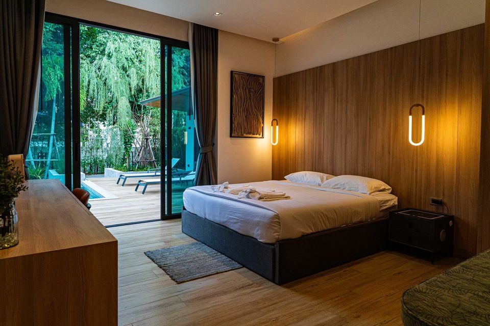 Bedroom with king-size bed, wooden headboard, and direct pool access at Sea Moment IV Pool Villa, Rayong.