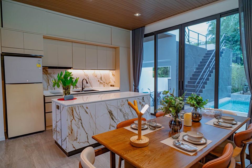 Modern dining table set for six next to a marble kitchen island at Sea Moment IV Pool Villa, Rayong.