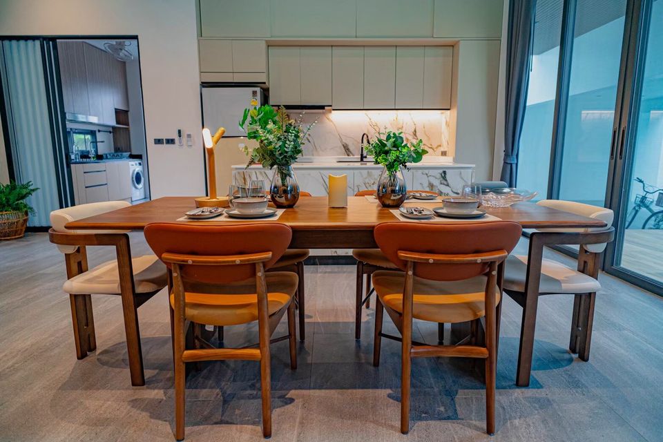 Modern dining table set for six with stylish chairs and kitchen view at Sea Moment IV Pool Villa, Rayong.