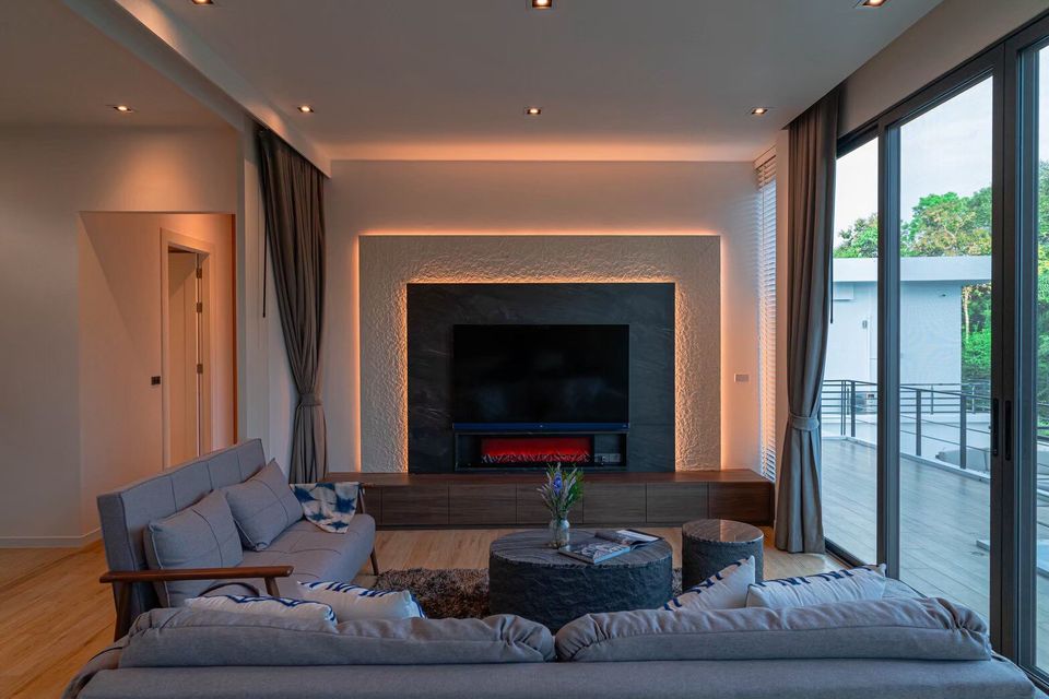 Modern living room at Sea Moment IV Pool Villa, Rayong, featuring a large TV, electric fireplace, and comfortable sofas.