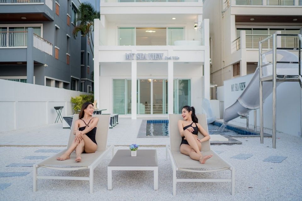 Two women lounge by the pool at Sea View IV Pool Villa in Pattaya. Waterslide visible. Relaxing poolside at this Thailand vil