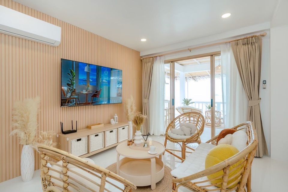Cozy living room at Story II Pool Villa Hua-Hin with rattan chairs, flat-screen TV, and sliding doors to a balcony.