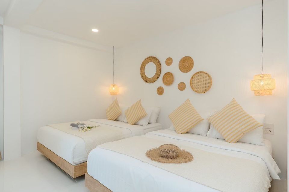 Bright bedroom at Story II Pool Villa Hua-Hin with two queen beds, striped pillows, and woven wall decor.