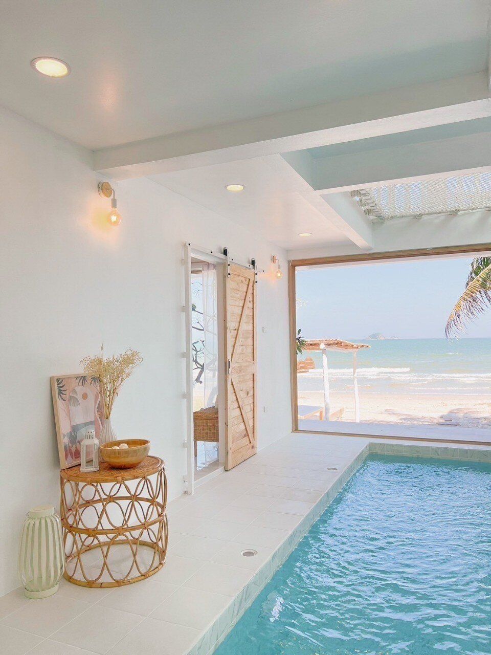 Indoor pool at Story II Pool Villa Hua-Hin, offering direct beachfront views and a cozy rattan side table.