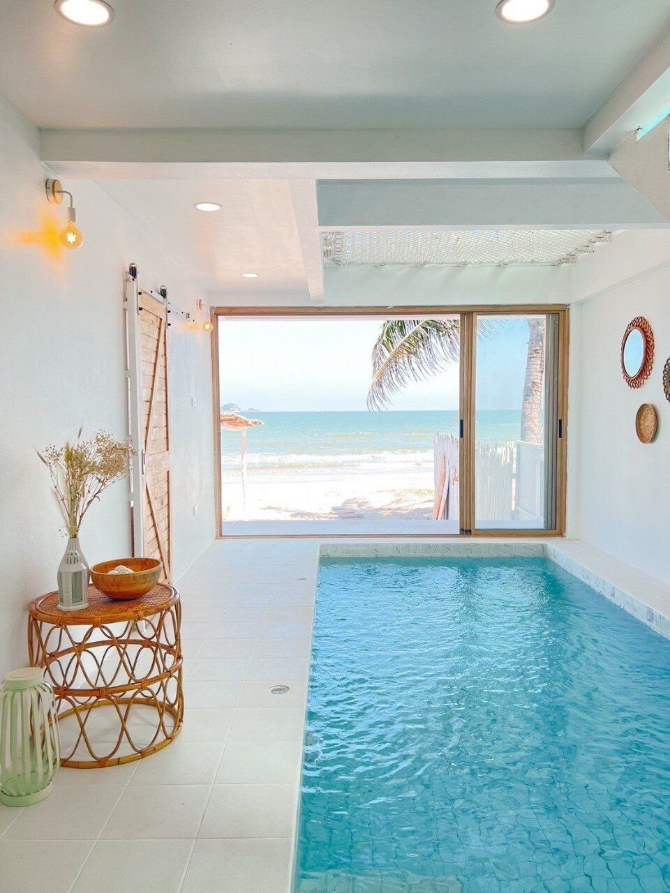 Indoor pool at Story II Pool Villa Hua-Hin, offering direct beachfront views and a cozy rattan side table.