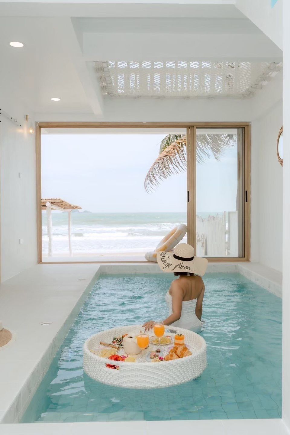 Woman enjoying a floating breakfast in the indoor pool at Story II Pool Villa Hua-Hin, with ocean views.