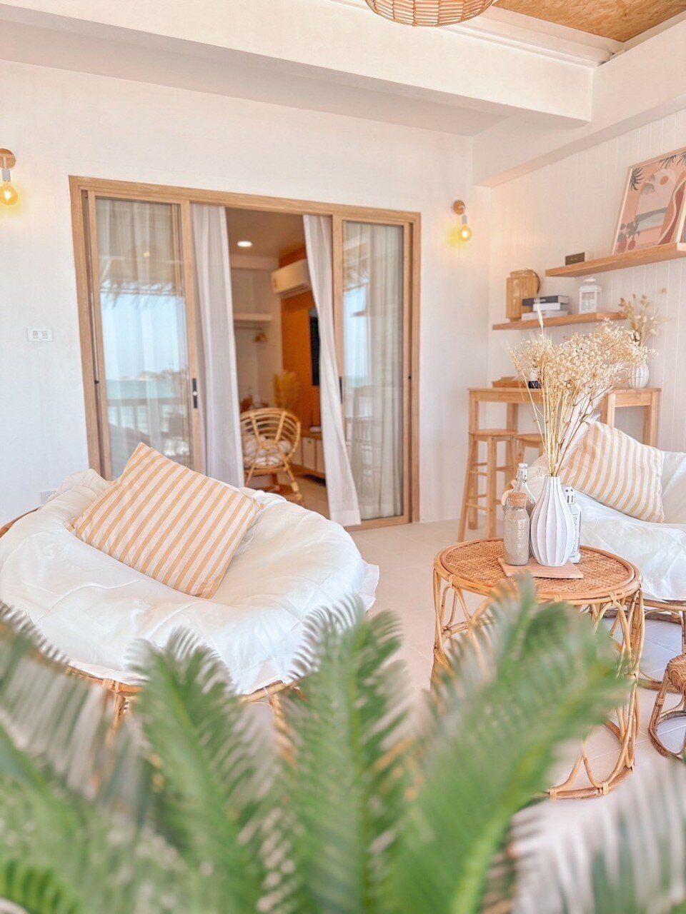 Bright living area with rattan chairs, striped pillows, and a view to the bedroom at Story II Pool Villa Hua-Hin.