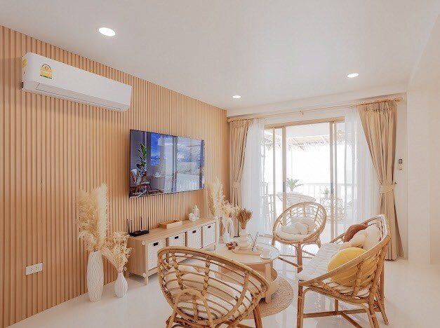Bright living room at Story II Pool Villa Hua-Hin with rattan chairs, TV, and sliding doors to a balcony.