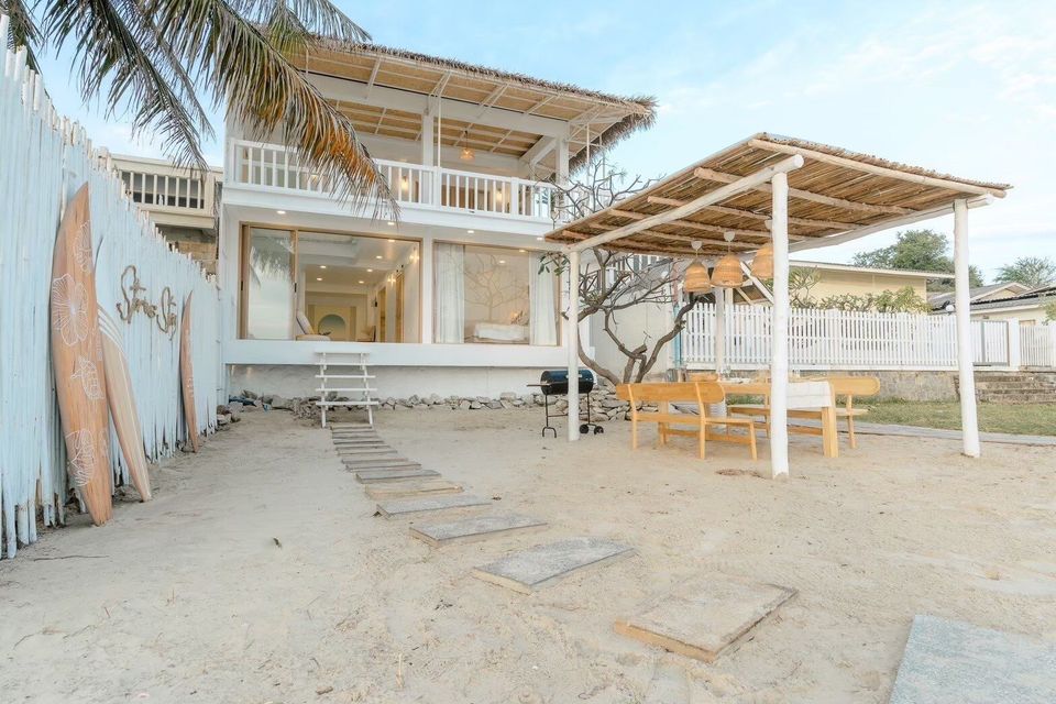 Story II Pool Villa Hua-Hin's beachfront exterior with a thatched roof, outdoor dining area, and BBQ grill on the sand.