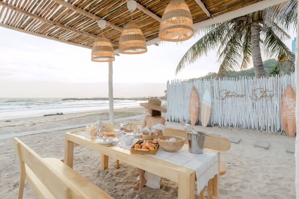 A woman enjoys breakfast at a beachfront dining table with ocean views at Story II Pool Villa Hua-Hin, Thailand.