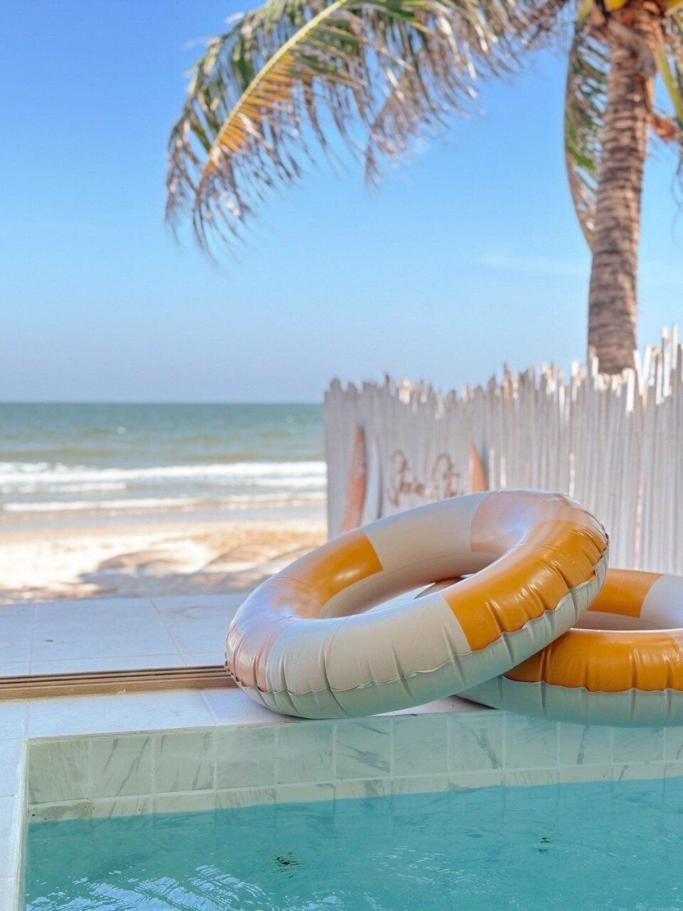 Orange and white pool floats by the private pool at Story II Pool Villa Hua-Hin, with the beach and ocean in the background.