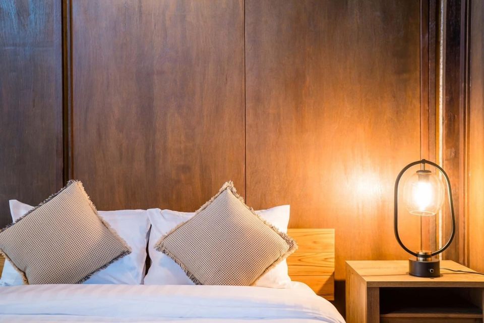 Close-up of a cozy bedroom at Studio Beachfront III Pool Villa, Cha-Am, featuring a modern bedside lamp and wooden headboard.