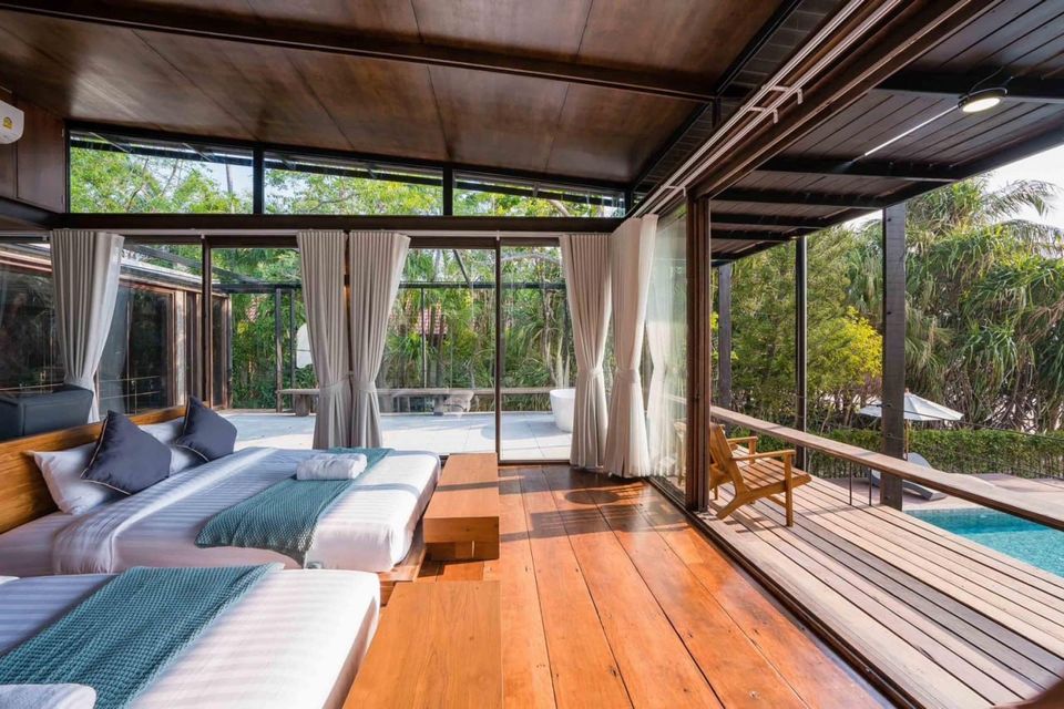 Bright bedroom with two twin beds, wooden floors, and a private balcony overlooking the pool at Studio Beachfront III Pool Villa, Cha-Am.