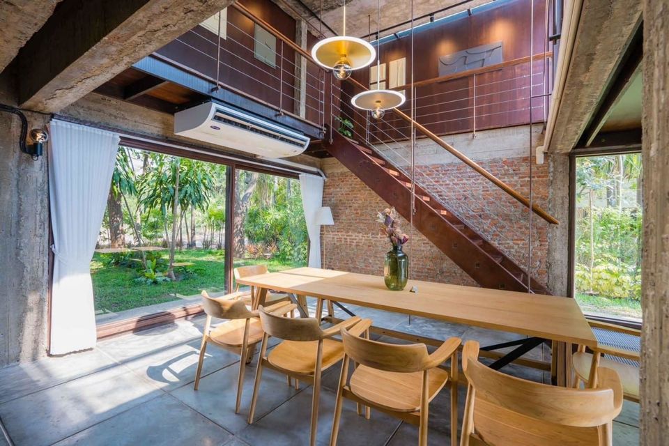 Indoor dining area at Studio Beachfront III Pool Villa, Cha-Am, with a long wooden table, chairs, and garden views.