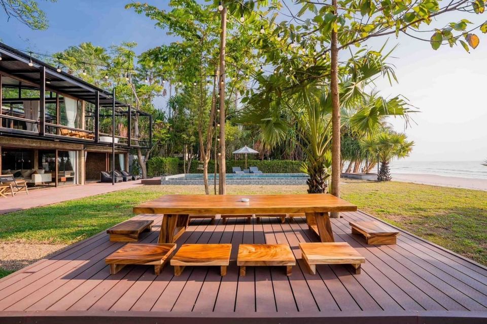 Outdoor wooden dining table and benches on a deck at Studio Beachfront III Pool Villa, Cha-Am, with pool and beach views.