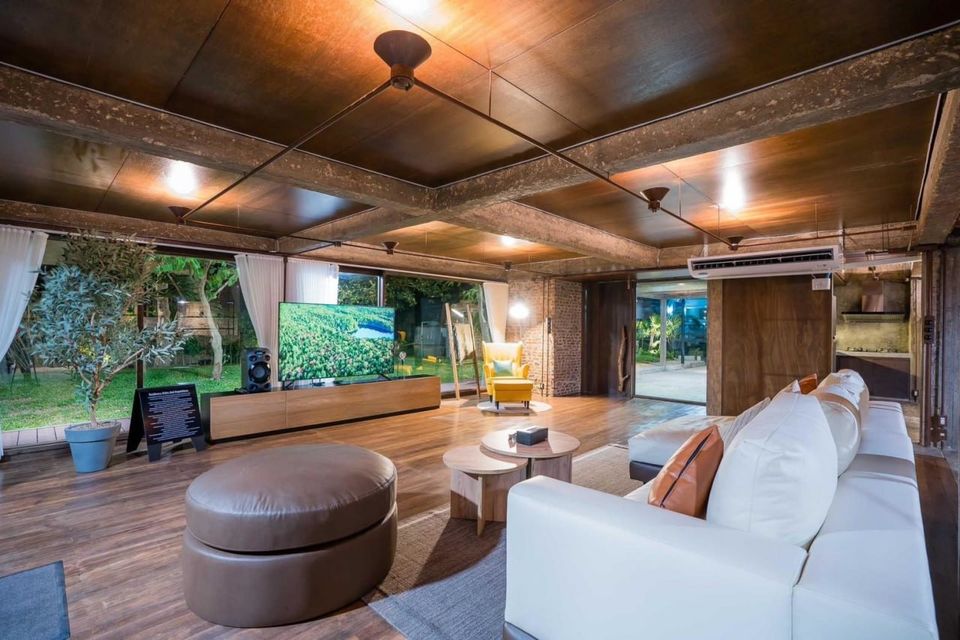 Spacious living room at Studio Beachfront III Pool Villa, Cha-Am, featuring a large TV, white sofa, and garden views.