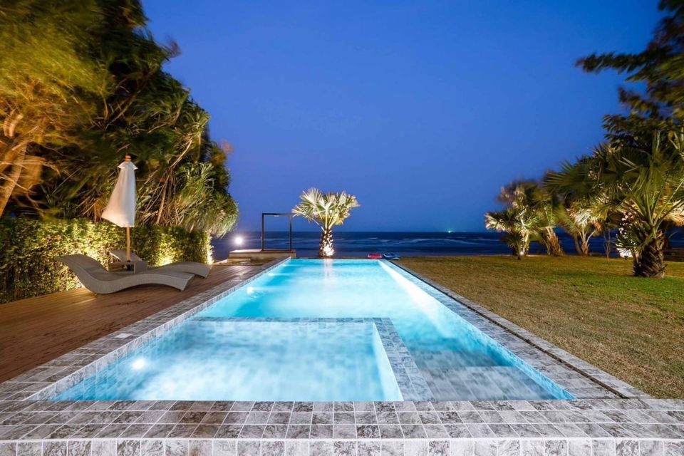 Illuminated pool at Studio Beachfront III Pool Villa, Cha-Am, with ocean view and palm trees under a clear night sky.