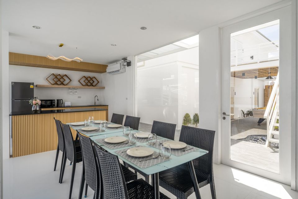 Indoor dining area with a glass table and black chairs, adjacent to a kitchenette at Talay Haus X Pool Villa, Cha-Am.