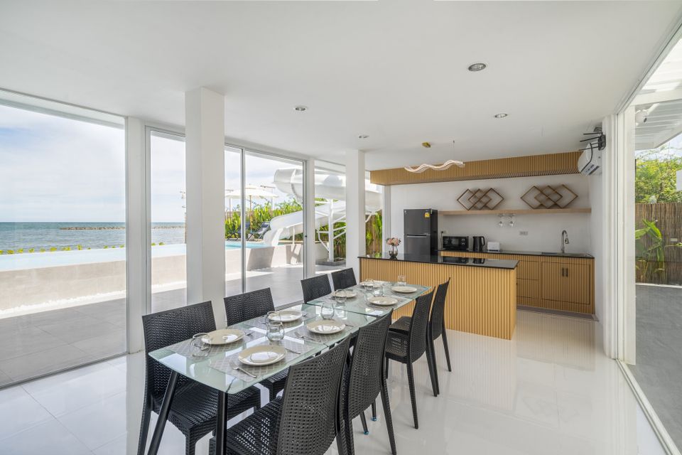 Indoor dining area at Talay Haus X Pool Villa, Cha-Am, with a glass table, black chairs, and ocean views.
