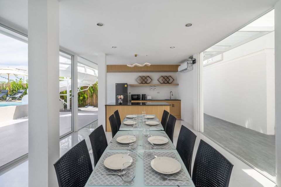Indoor dining area at Talay Haus X Pool Villa, Cha-Am, with a long table set for guests and a view of the pool and water slide.