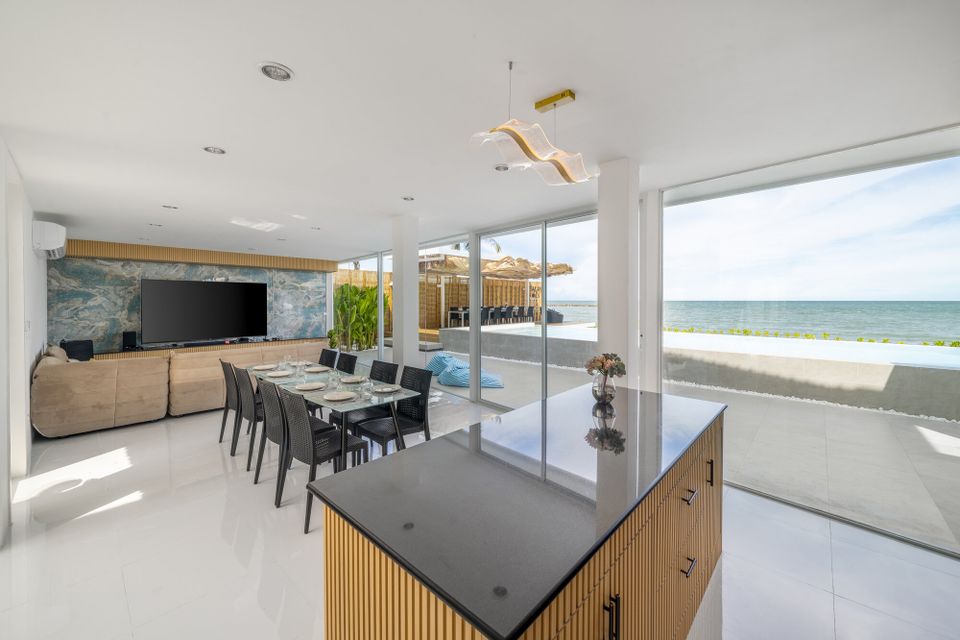 Spacious open-plan dining area at Talay Haus X Pool Villa, Cha-Am, with a long table, modern kitchen island, and stunning ocean views.