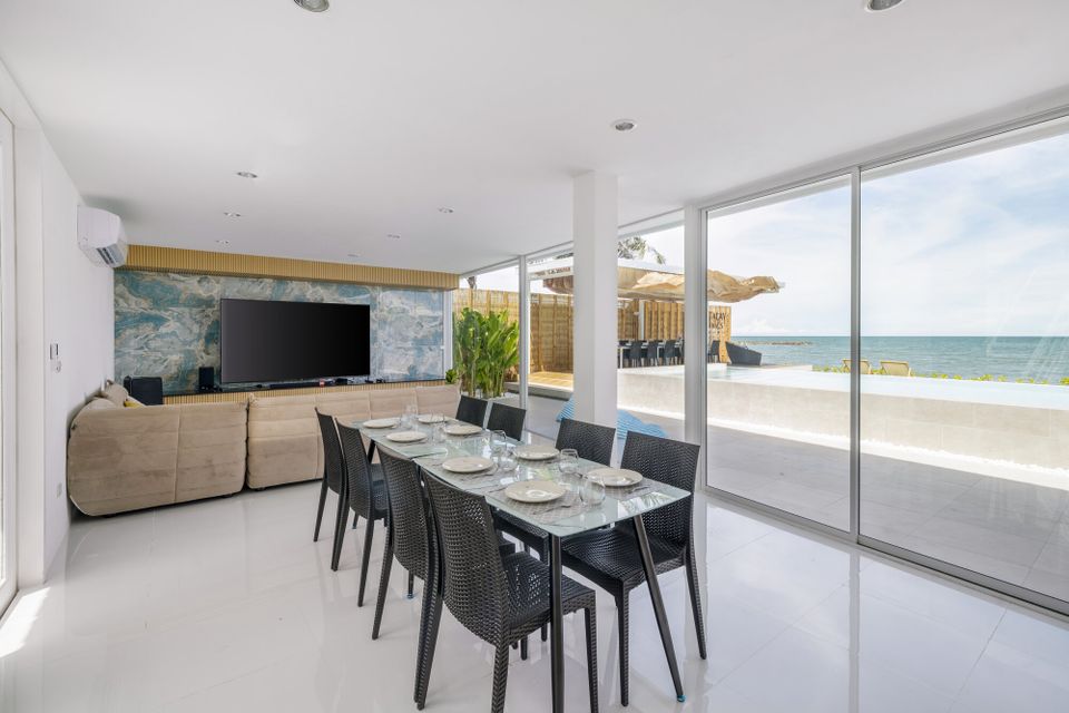 Indoor dining area at Talay Haus X Pool Villa, Cha-Am, with a glass table, black chairs, and ocean views.