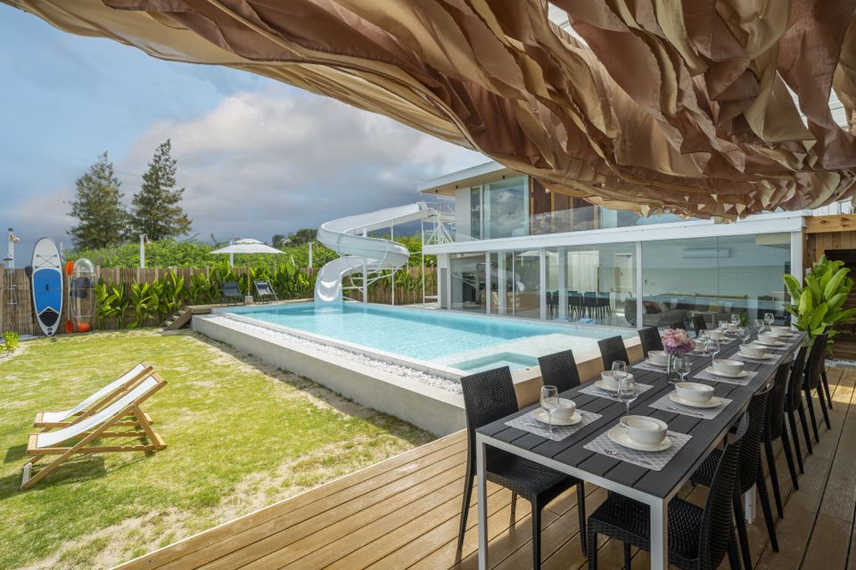 Outdoor dining table set for guests at Talay Haus X Pool Villa in Cha-Am, with pool and water slide in background.
