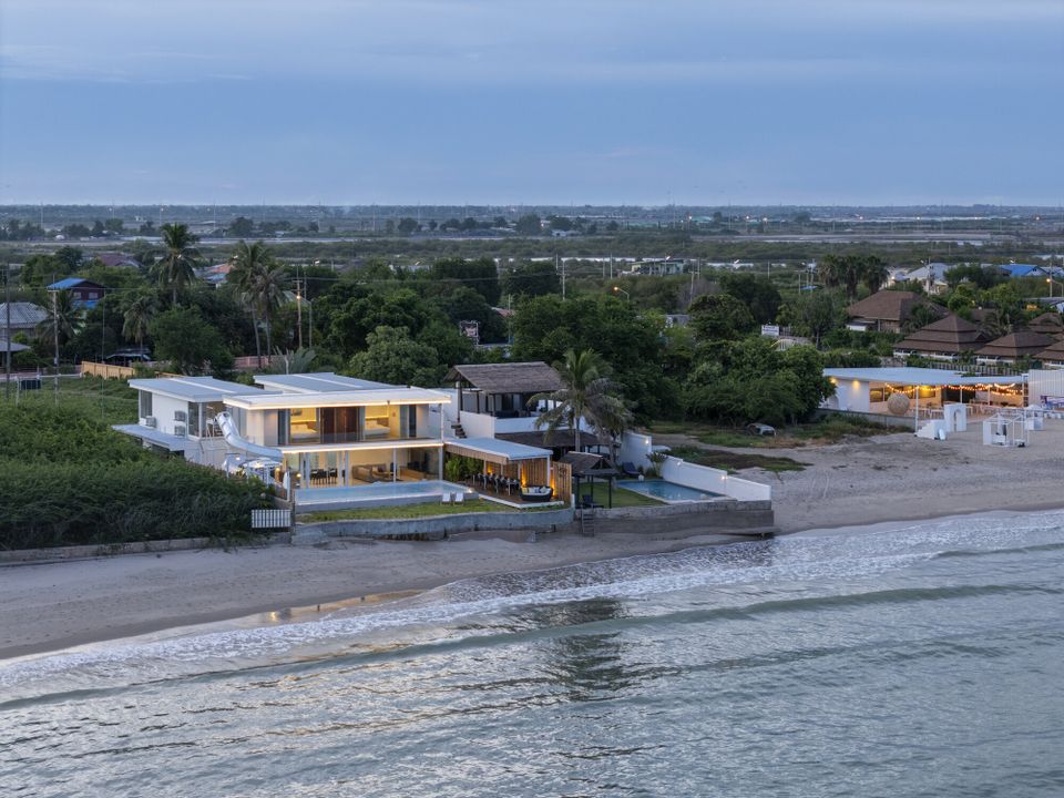 Aerial view of Talay Haus X Pool Villa in Cha-Am at dusk, showcasing its modern design, beachfront location, and illuminated interiors.