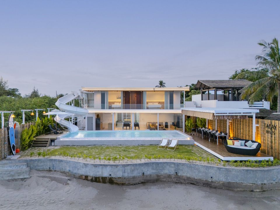 Aerial view of Talay Haus X Pool Villa in Cha-Am, showing the modern beachfront villa, pool, water slide, and outdoor dining area at dusk.
