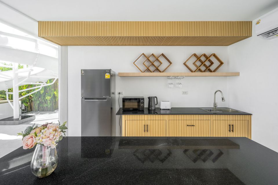 Modern kitchen at Talay Haus X Pool Villa, Cha-Am, featuring a black granite island, wood cabinetry, and stainless steel appliances.