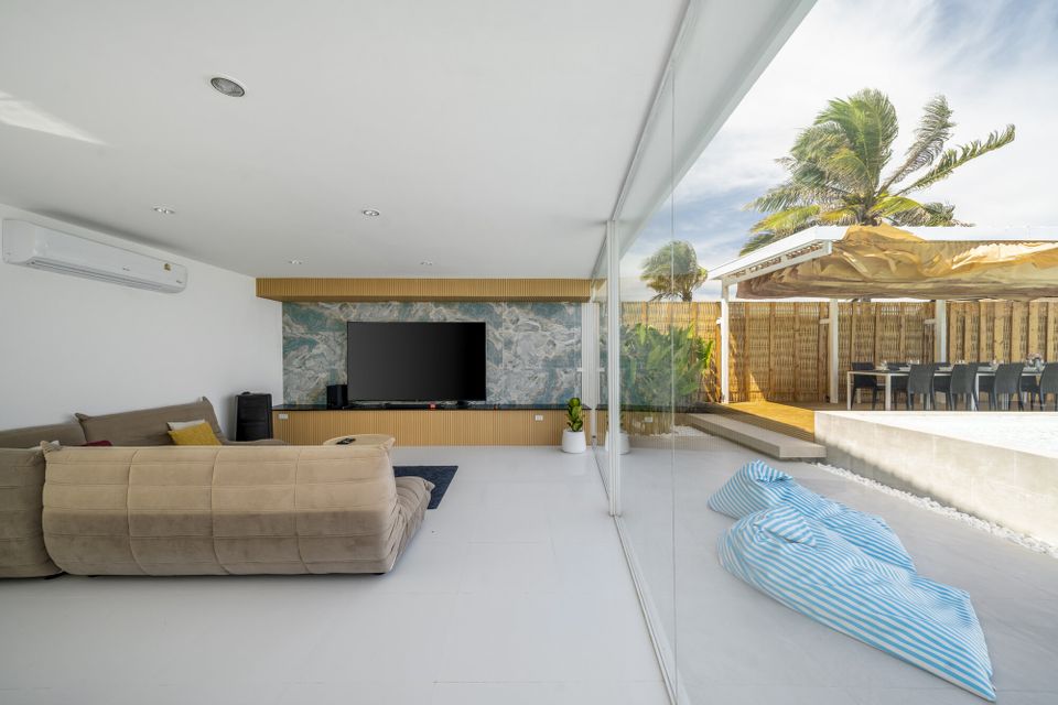 Spacious living room at Talay Haus X Pool Villa, Cha-Am, with large TV, comfortable sofa, and glass doors opening to outdoor dining.
