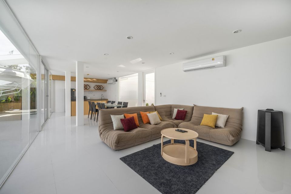 Bright living room at Talay Haus X Pool Villa, Cha-Am, featuring a modern sectional sofa with colorful pillows and a wooden coffee table.