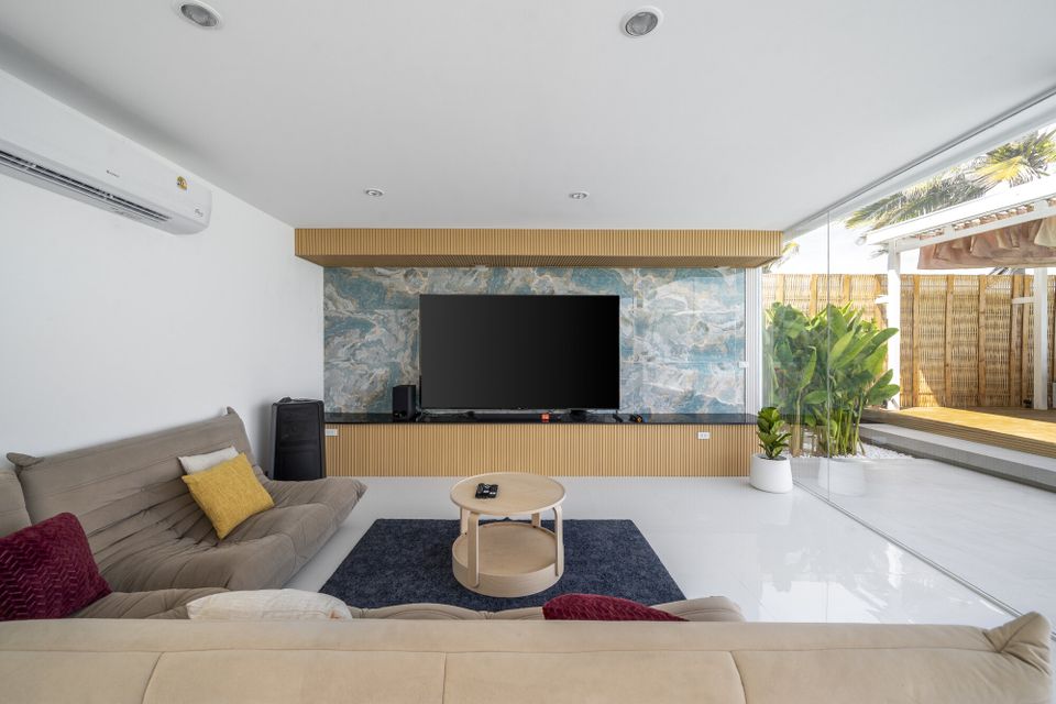 Modern living room at Talay Haus X Pool Villa, Cha-Am, featuring a large TV, comfortable sofas, and a view of the outdoor patio.