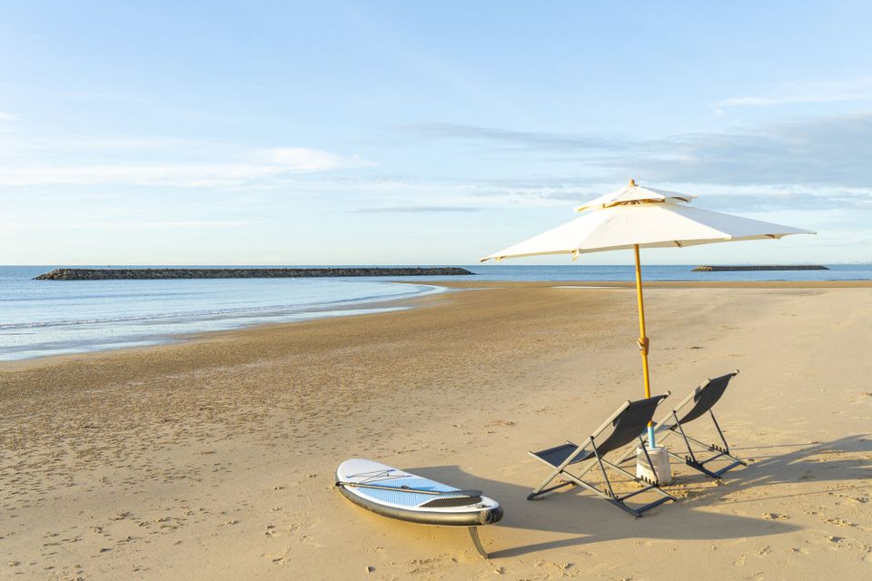 Paddleboard, beach chairs, and umbrella on the sandy beach at Talay Haus X Pool Villa, Cha-Am, with ocean views.