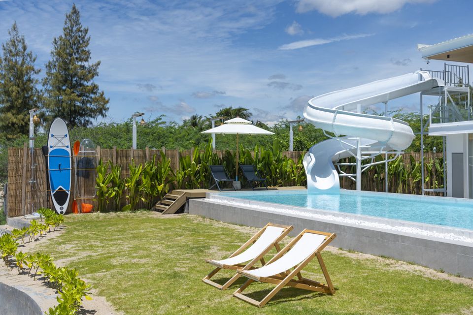 The Talay Haus X Pool Villa in Cha-Am features a large outdoor swimming pool with a white water slide and sun loungers.