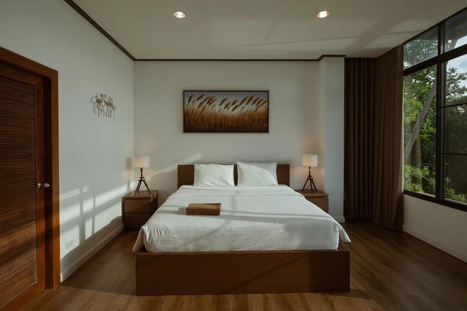 Spacious bedroom with a comfortable king-size bed, wooden furniture, and large window overlooking lush forest at The Valley Khaoyai V Villa.
