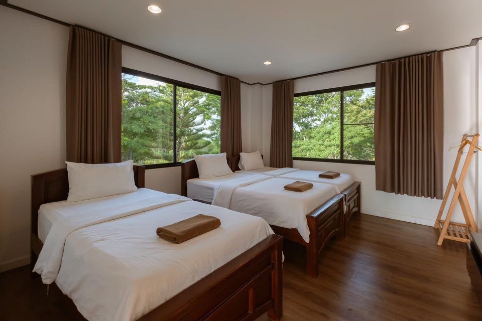 Bedroom with three single beds, white linens, and large windows overlooking lush greenery at The Valley Khaoyai V Villa.